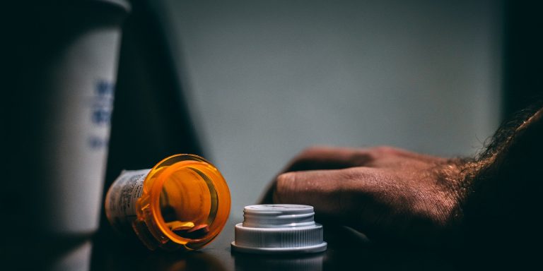 Behind the Opioid Epidemic 8 Orange and White Prescription Bottle On Table, suggesting the opioid epidemic