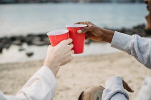 Whistleblower News 2 People Touching Red Solo Cups Together on a Beach