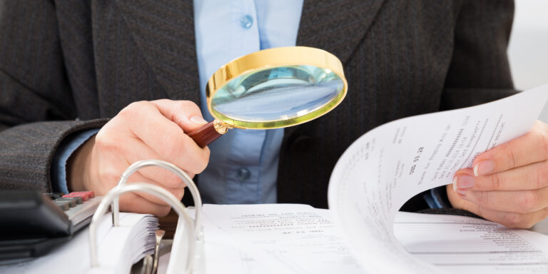 Caremark Fraud and Its Impact on the PBM Industry 11 Close-up Of Businessperson Checking Bills With Magnifying Glass, representing Caremark Fraud